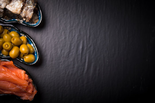 Fish assortment and olives on a plate on a dark background. With