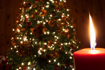 Red candle burning in front of a decorated Christmas tree with all the lights on