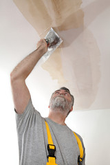 Worker repairing plaster at ceiling with trowel