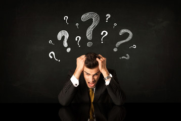 Sitting businessman under question marks