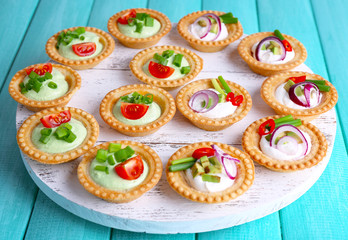 Tartlets with greens and vegetables with sauce on tray on table