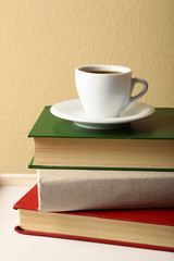 Pile of books with cup on tabletop and light wall background