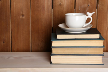 Pile of books with cup on tabletop and wooden background