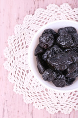 Prunes in bowl on lace doily on color wooden background