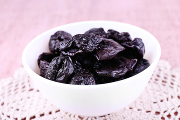 Prunes in bowl on lace doily on color wooden background