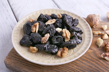 Wooden board with plate of prunes and walnuts