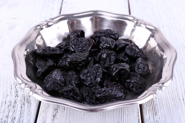 Metal plate of prunes on color wooden background