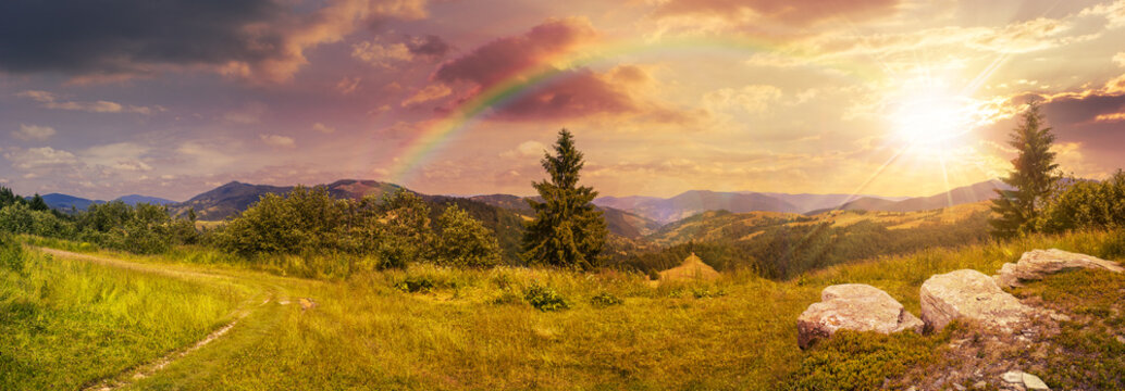 boulders on hillside meadow in mountain at sunset with rainbow