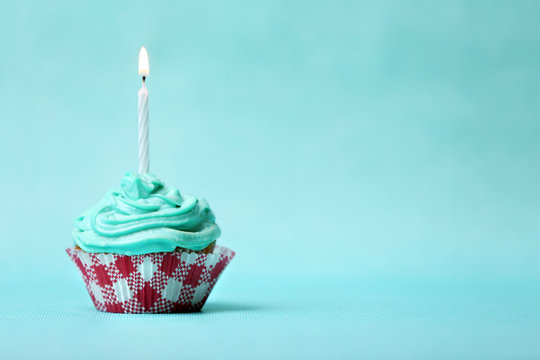 Delicious birthday cupcake on table on light green background