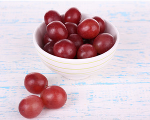Bowl of red grapes on color wooden surface on white background