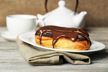 Tasty eclairs and cup of tea on wooden table