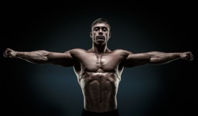 Fototapeta na wymiar Handsome muscular bodybuilder posing and keeping arms outstretch