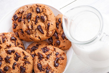 Chocolate cookies and milk in jug on white wood background