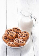 Chocolate cookies and milk in jug on white wood background