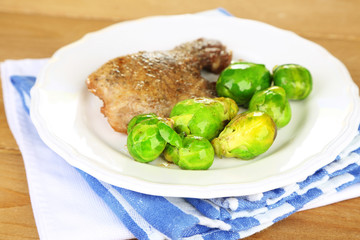 Roasted meat and vegetables on plate, on wooden table