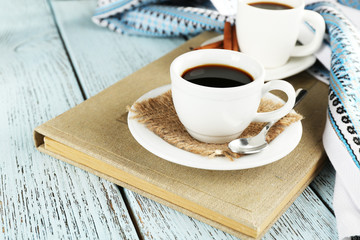 Cups of coffee on book on color wooden background