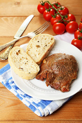 Roasted meat and vegetables on plate, on wooden table