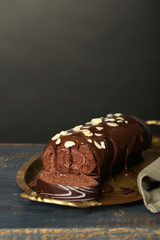 Delicious roll cake on wooden table, on dark background