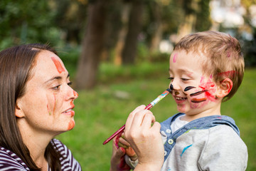Happy mother painting her child´s face in the park