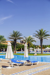 swimming pool with sun loungers, parasols and palm trees