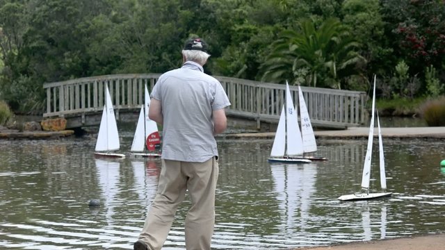 People sail remote control sailing wooden yachts in a pond