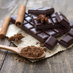 Broken chocolate bar and spices on wooden table.