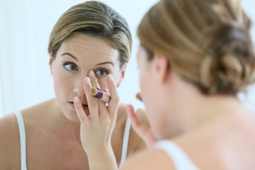 Beautiful blond woman applying concealer around eyes