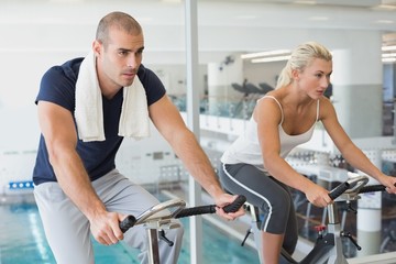 Fototapeta na wymiar Determined couple working on exercise bikes at gym