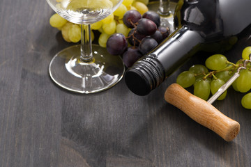 bottle of red wine and grapes on a wooden background, close-up