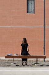 Fototapeta na wymiar Gorgeous girl in black dress looking at brick wall while sitting