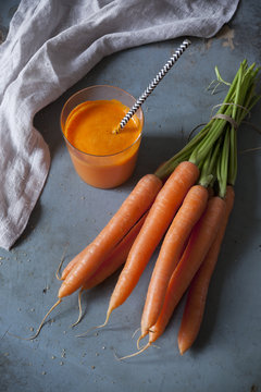 carrot smoothie on glass with straw and carrots bunch on table