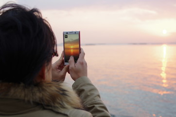 スマートフォンで初日の出を撮影する男性