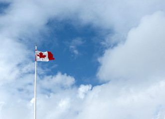 The maple leaf flies high against a background of fluffy clouds.