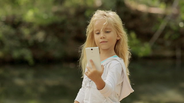 Little girl makes the photo on the phone in the forest near the