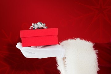 Composite image of hand of santa claus holding a gift