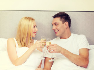 Obraz na płótnie Canvas smiling couple with champagne glasses in bed