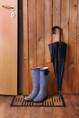 Fototapeta premium Dirty wellington boots with umbrella on door mat in room