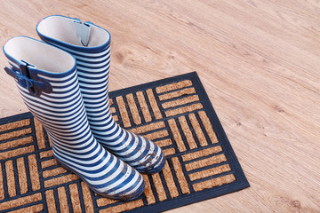 Naklejka premium Dirty wellington boots on door mat in room