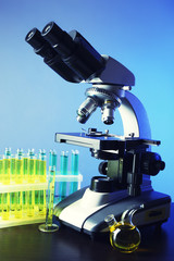 Microscope and test tubes on table, on color background