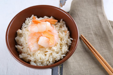 Boiled rice and shrimps in bowl, on wooden background
