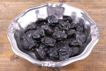 Metal plate of prunes on wooden background