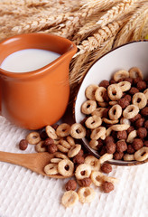 Various sweet cereals in ceramic bowl, fruits and jug with milk