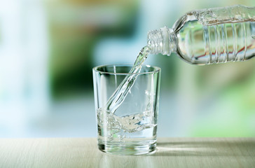 Pouring water from bottle on  glass on light background