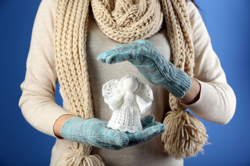 Knitted Christmas angel in female hand on color background
