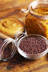 Mustard seeds and sauce in glass jar, bowls on wooden