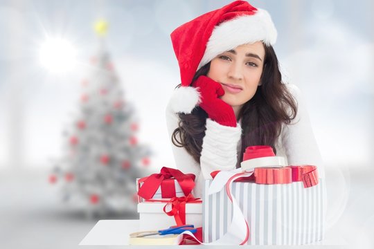 Composite image of unsure brunette in santa hat packing gifts