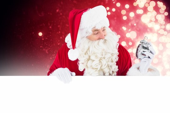 Composite image of happy santa holding alarm clock and sign