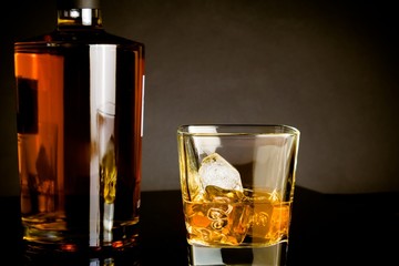 whiskey with ice in glass near bottle on dark background