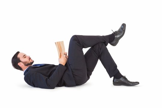 Businessman lying on the floor reading a book
