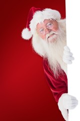 Composite image of santa looks out behind a wall